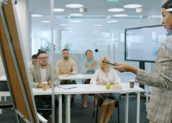 Managers men and women are listening to employee young lady making report in conference room talking and gesturing using flipchart whiteboard.