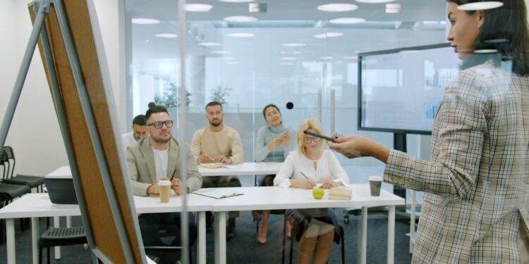 Managers men and women are listening to employee young lady making report in conference room talking and gesturing using flipchart whiteboard.