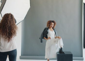 African-American woman model working with stylist and photographer indoors in studio wearing trendy clothing and headwear. People and photography concept.