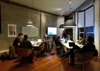 group of adult students sitting at a large table working on computers and discussing