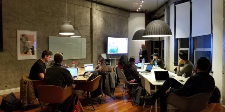 group of adult students sitting at a large table working on computers and discussing