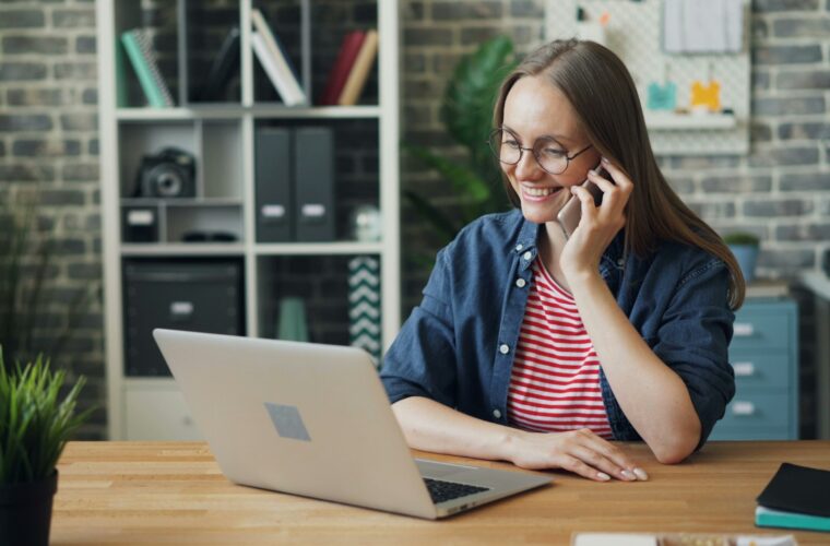 Vrouw belt zakelijk met haar mobiele telefoon achter een laptop