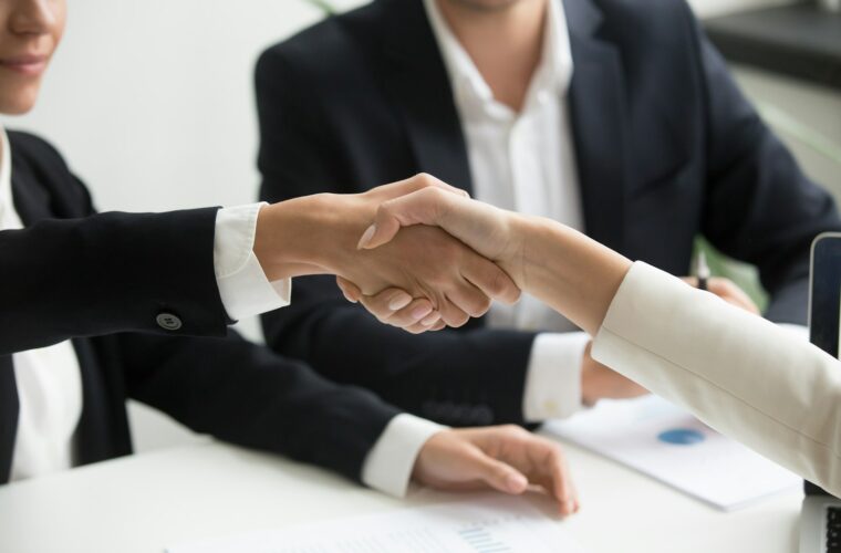 Twee ondernemers geven elkaar een hand boven een getekend contract
